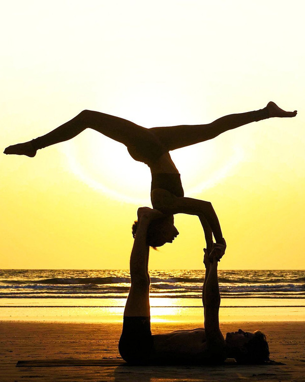 AcroYoga Couple at the Beach at Sunrise holding female in the air in the upside down splits.