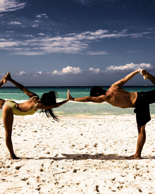 Partner beach yoga in Florida. Man and a woman in Dancer Yoga Pose Asana touching hands.
